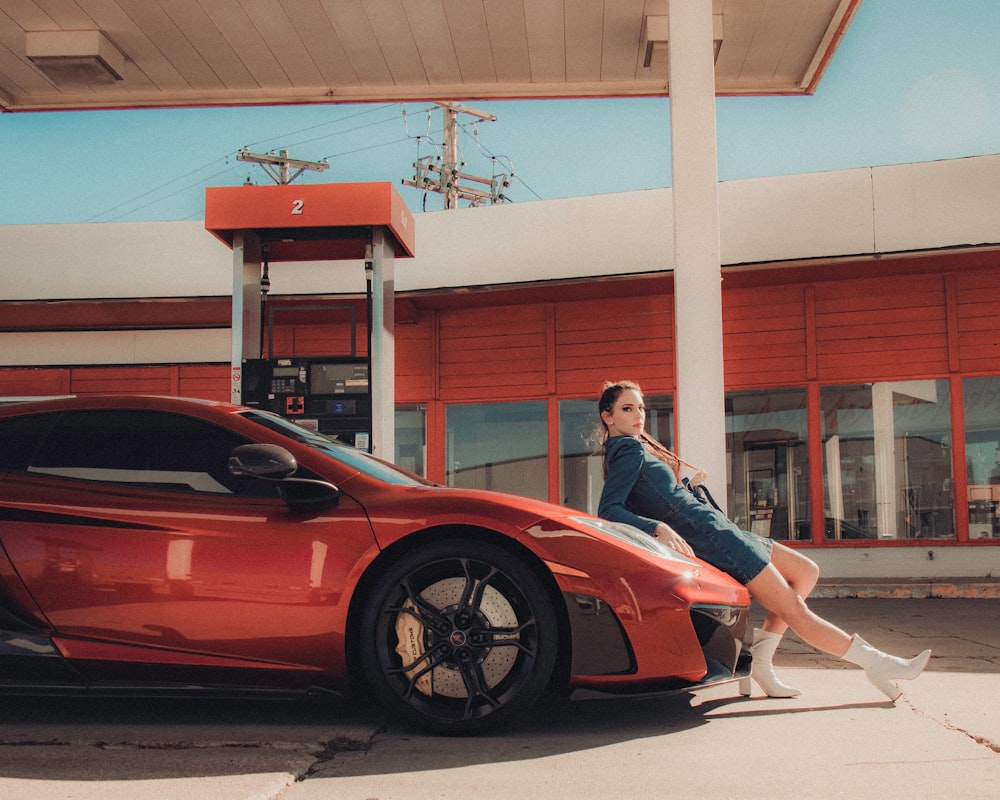 Mujer con chaqueta negra y pantalones blancos de pie junto a Ferrari Coupé rojo