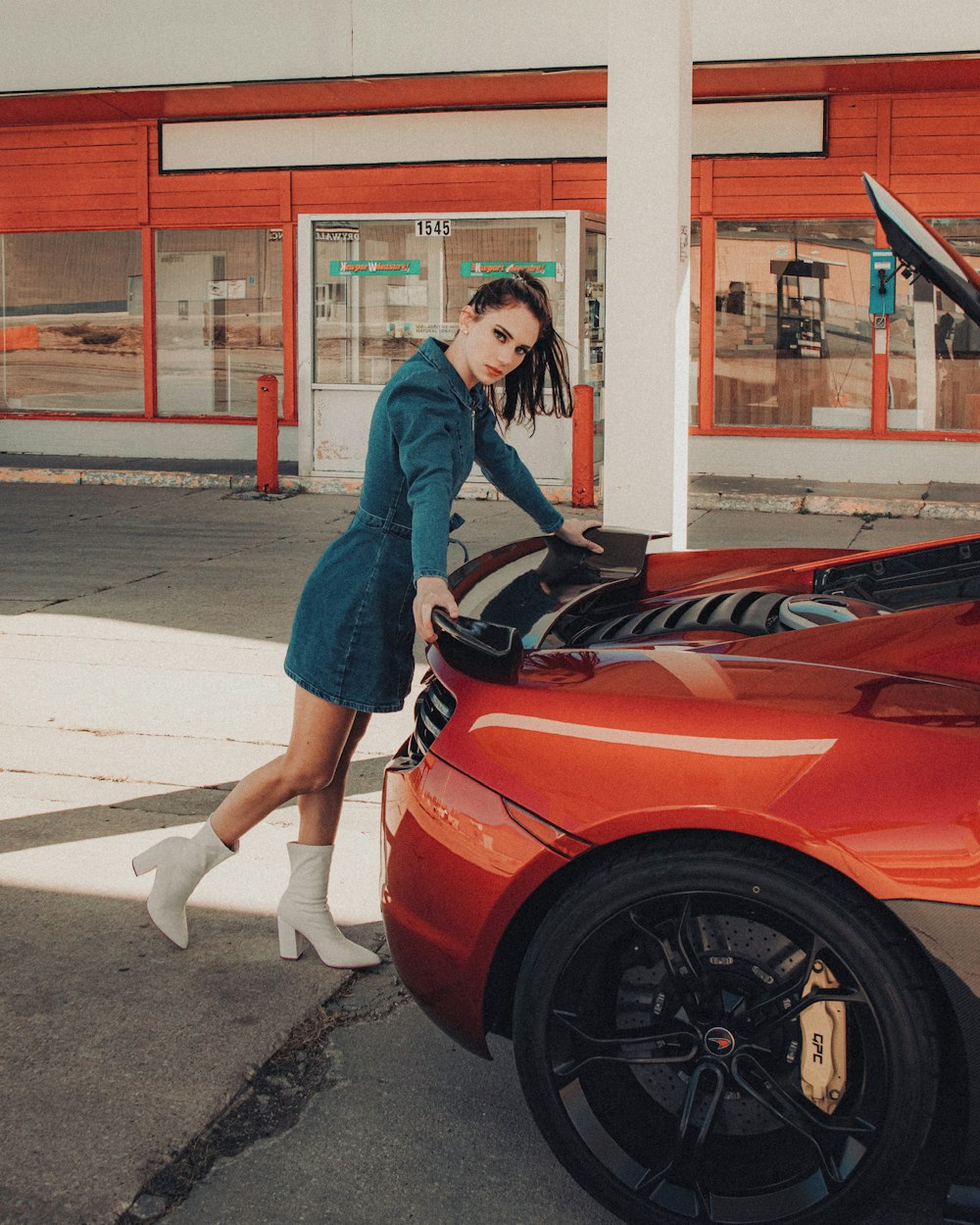 woman in blue denim jacket and white pants standing beside red ferrari car