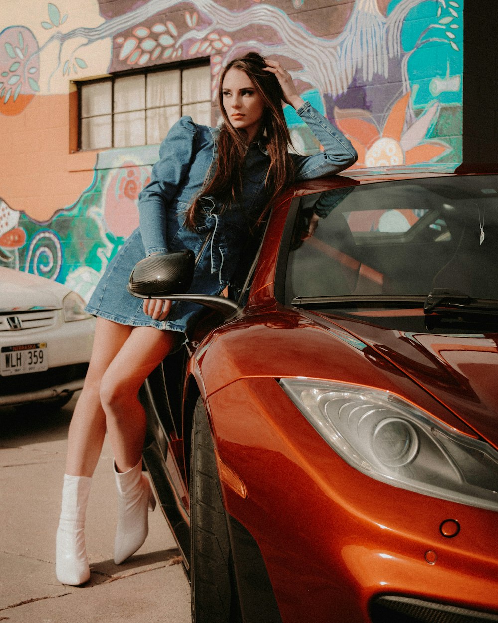 woman in blue denim jacket standing beside red car