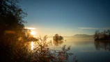 Sunrise over a tranquil lake with silhouettes of travelers enjoying the view.