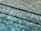 Rippling water in a swimming pool creates patterns of light and shadow. Black lane markers run horizontally across the pool, partially submerged and creating distinct lines against the clear blue water.
