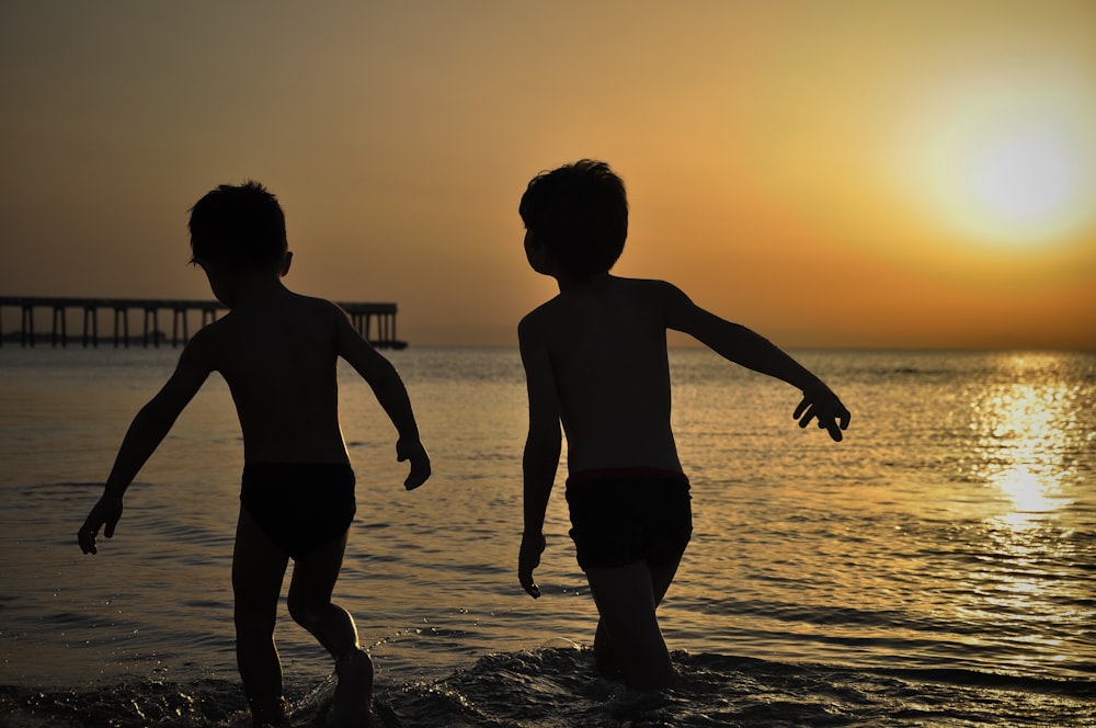 2 boys standing on beach during sunset