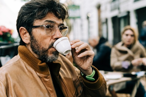 Homme en veste marron buvant un expresso dans une tasse en céramique blanche.
