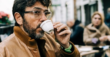 man in brown jacket drinking on white ceramic mug