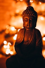 A serene backlit bronze lotus and Buddha surrounded by soft light.