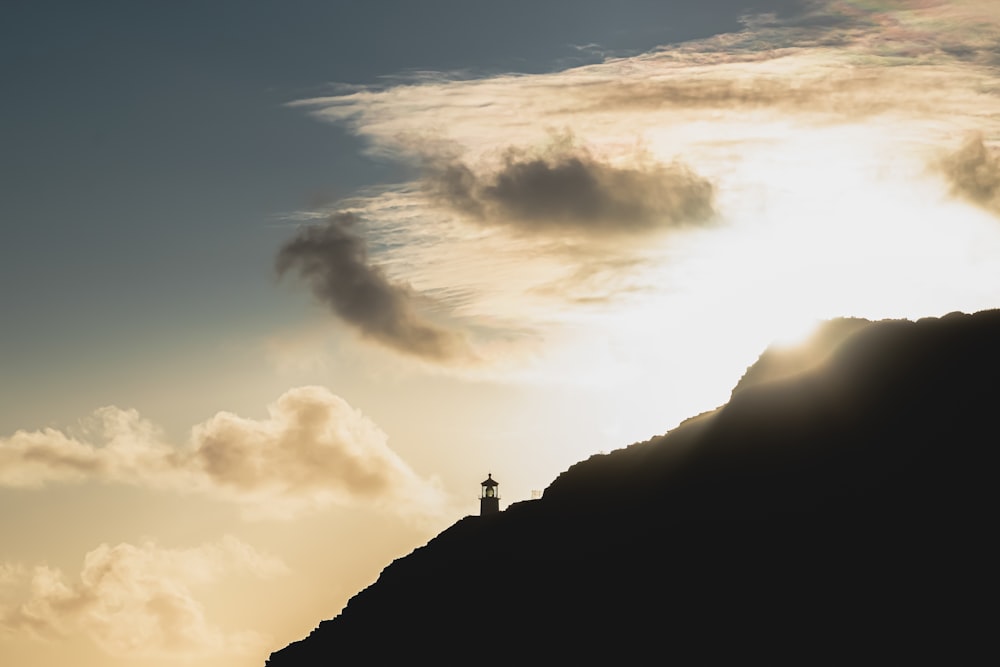silhueta da pessoa em pé no topo da montanha sob o céu nublado durante o dia
