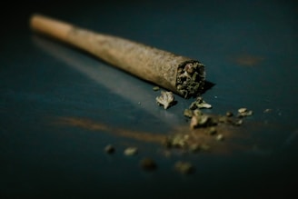 Close-up photo of a cannabis joint resting on a rustic wooden table with soft natural light highlighting the texture.