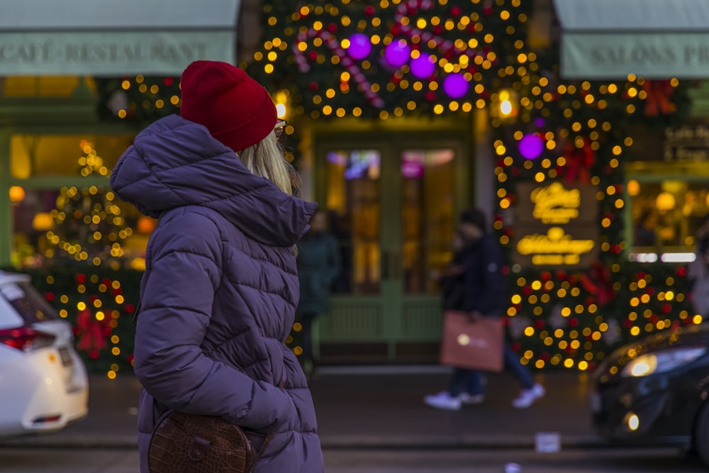 woman in red knit cap and black jacket standing on sidewalk during night time