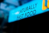 Text displaying the phrase 'NATURALLY FAST FOOD' is shown against a blue background. The lettering is black and the word arrangement suggests a focus on natural and quick meal options.