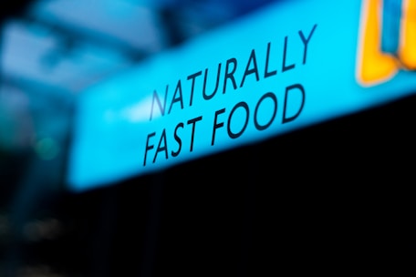 Text displaying the phrase 'NATURALLY FAST FOOD' is shown against a blue background. The lettering is black and the word arrangement suggests a focus on natural and quick meal options.