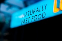 Text displaying the phrase 'NATURALLY FAST FOOD' is shown against a blue background. The lettering is black and the word arrangement suggests a focus on natural and quick meal options.