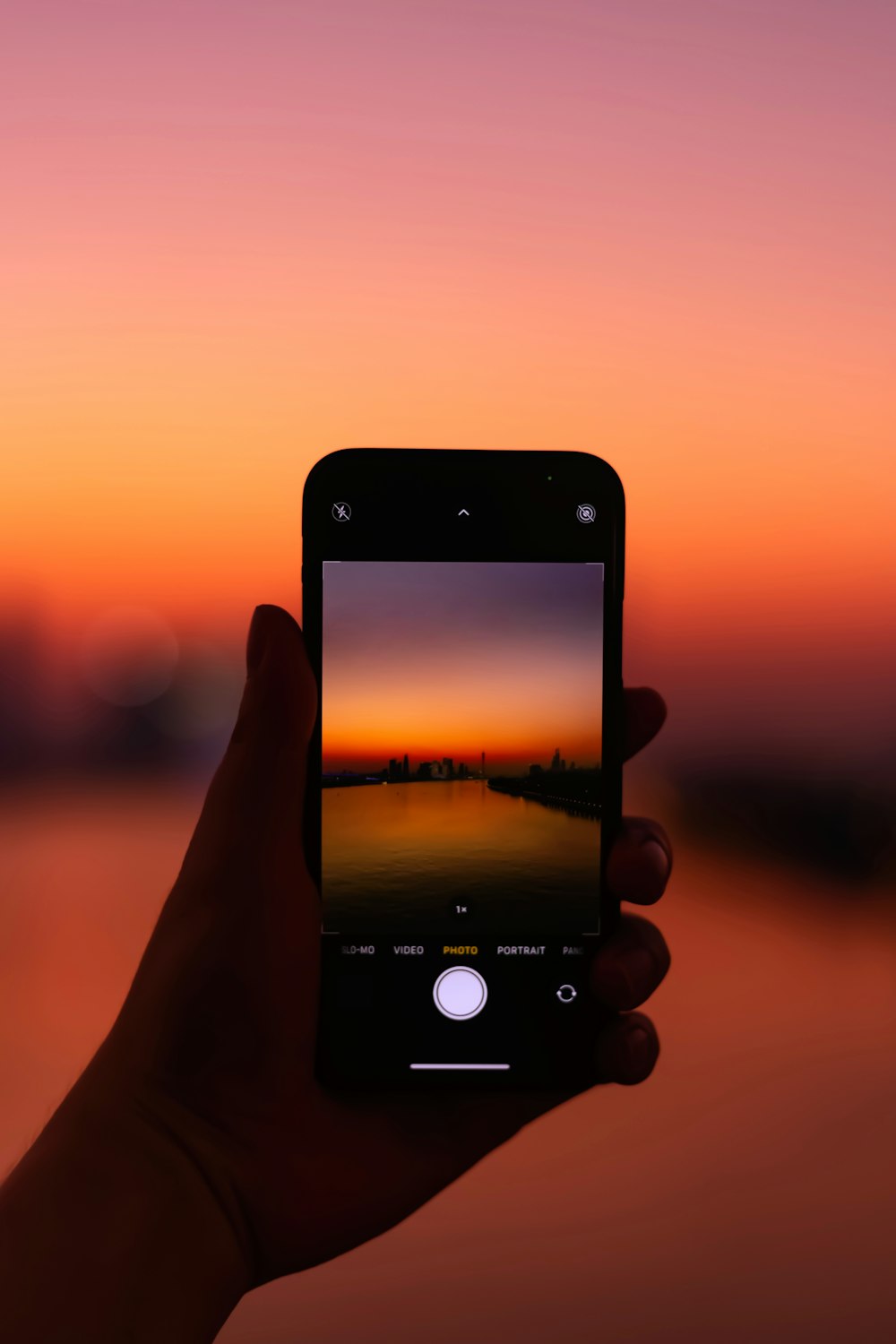 person holding iphone taking photo of sunset