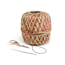 A multicolored ball of yarn is placed alongside a pair of small scissors and a crochet hook. The yarn features a pattern with red, green, and white strands intricately wrapped around in layers. The scissors have metal blades and golden handles, while the crochet hook is silver and slender.