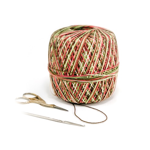 A multicolored ball of yarn is placed alongside a pair of small scissors and a crochet hook. The yarn features a pattern with red, green, and white strands intricately wrapped around in layers. The scissors have metal blades and golden handles, while the crochet hook is silver and slender.
