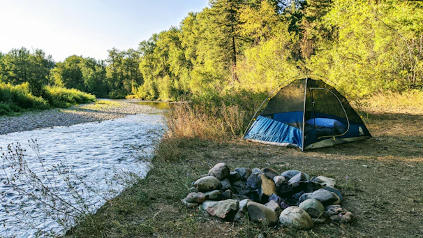A cozy riverside campsite glowing warmly with a bonfire and tents nestled among trees.