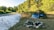 A cozy camper setup beside a fire pit with a scenic river and lush grass in the background.