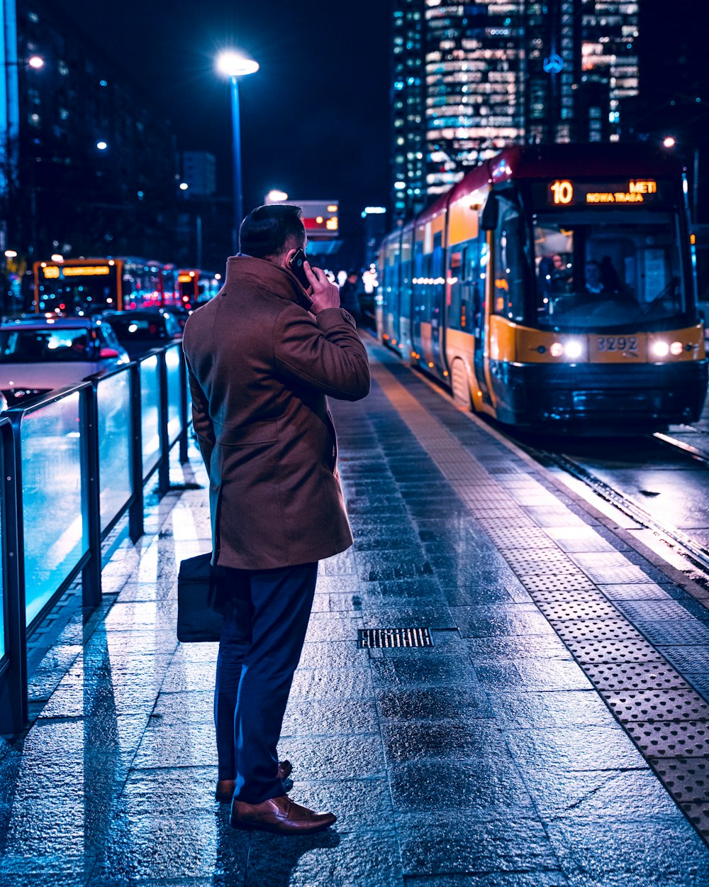 man in brown coat standing on sidewalk near train