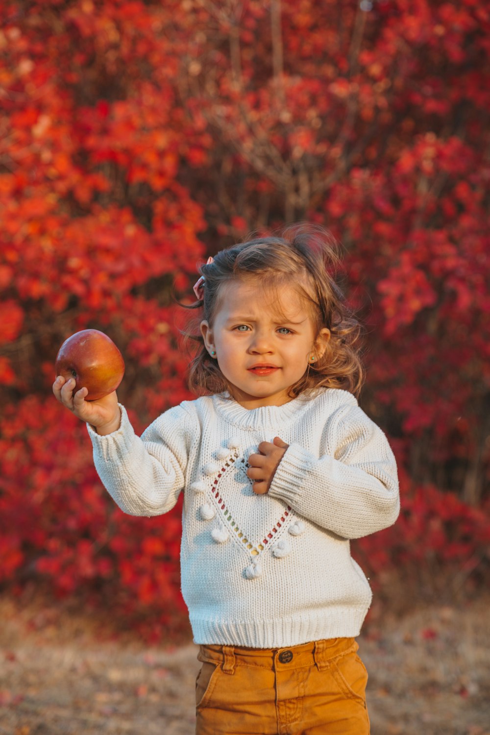girl in white sweater holding brown round fruit