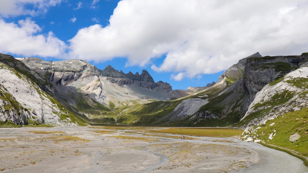 campo de grama verde perto da montanha sob nuvens brancas e céu azul durante o dia