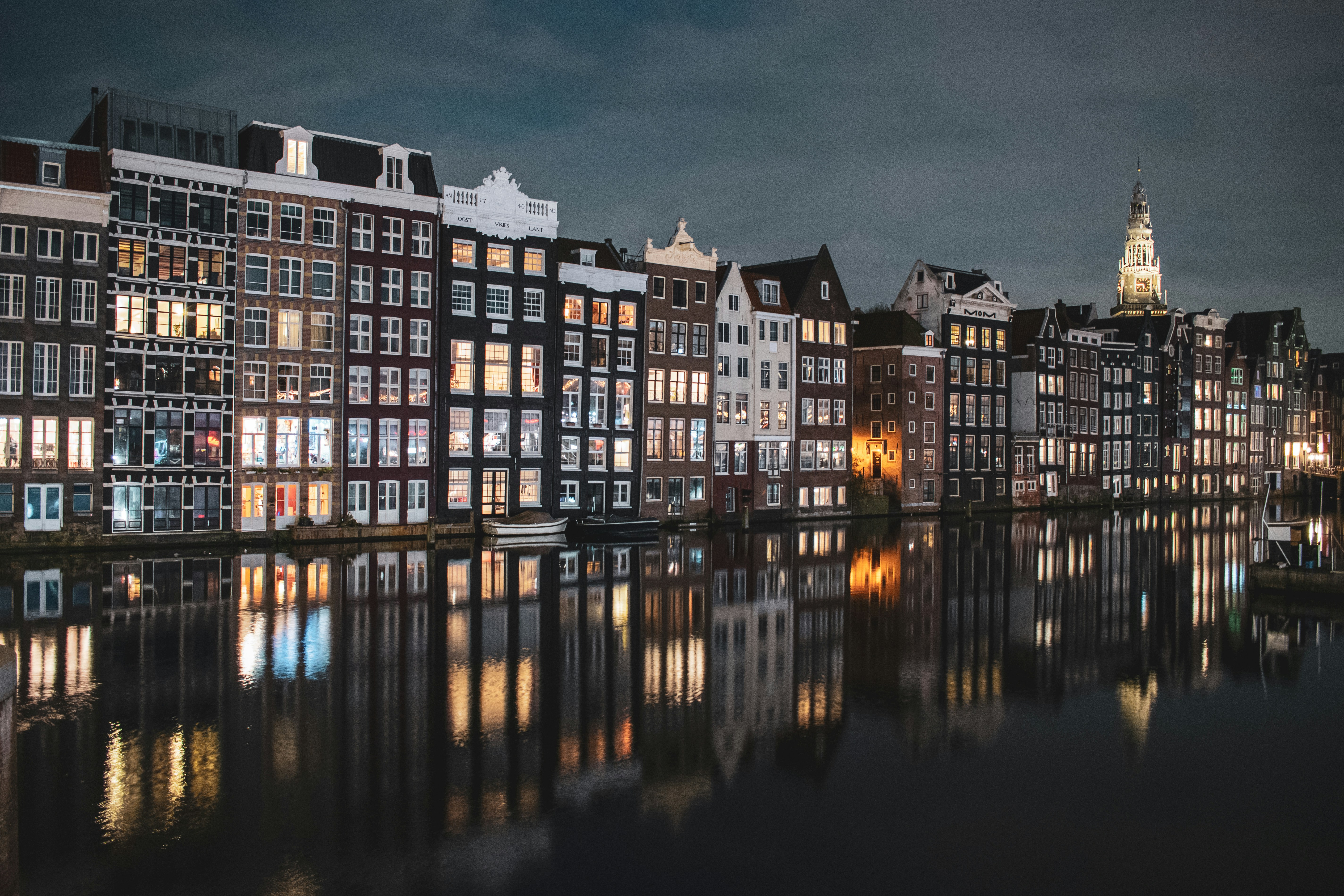 brown and white concrete building near body of water during night time, A classic evening sight in Amsterdam.