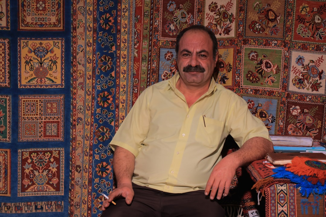 man in white polo shirt and black pants sitting on red and blue floral textile