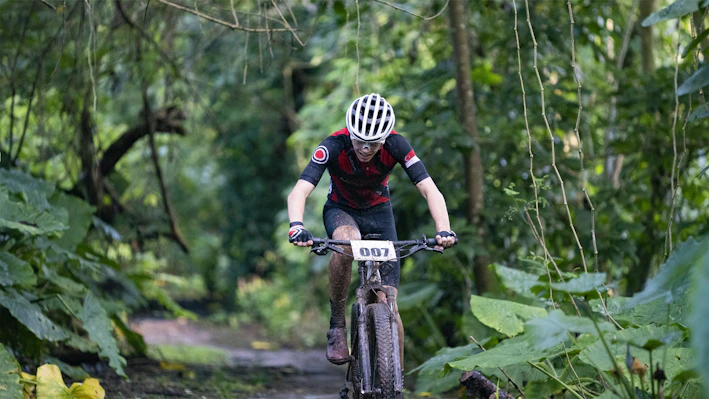 A cyclist wearing a bright helmet and gloves riding on a forest trail