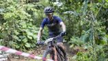 Cyclist climbing a steep, dusty mountain trail surrounded by lush greenery in Minas Gerais.