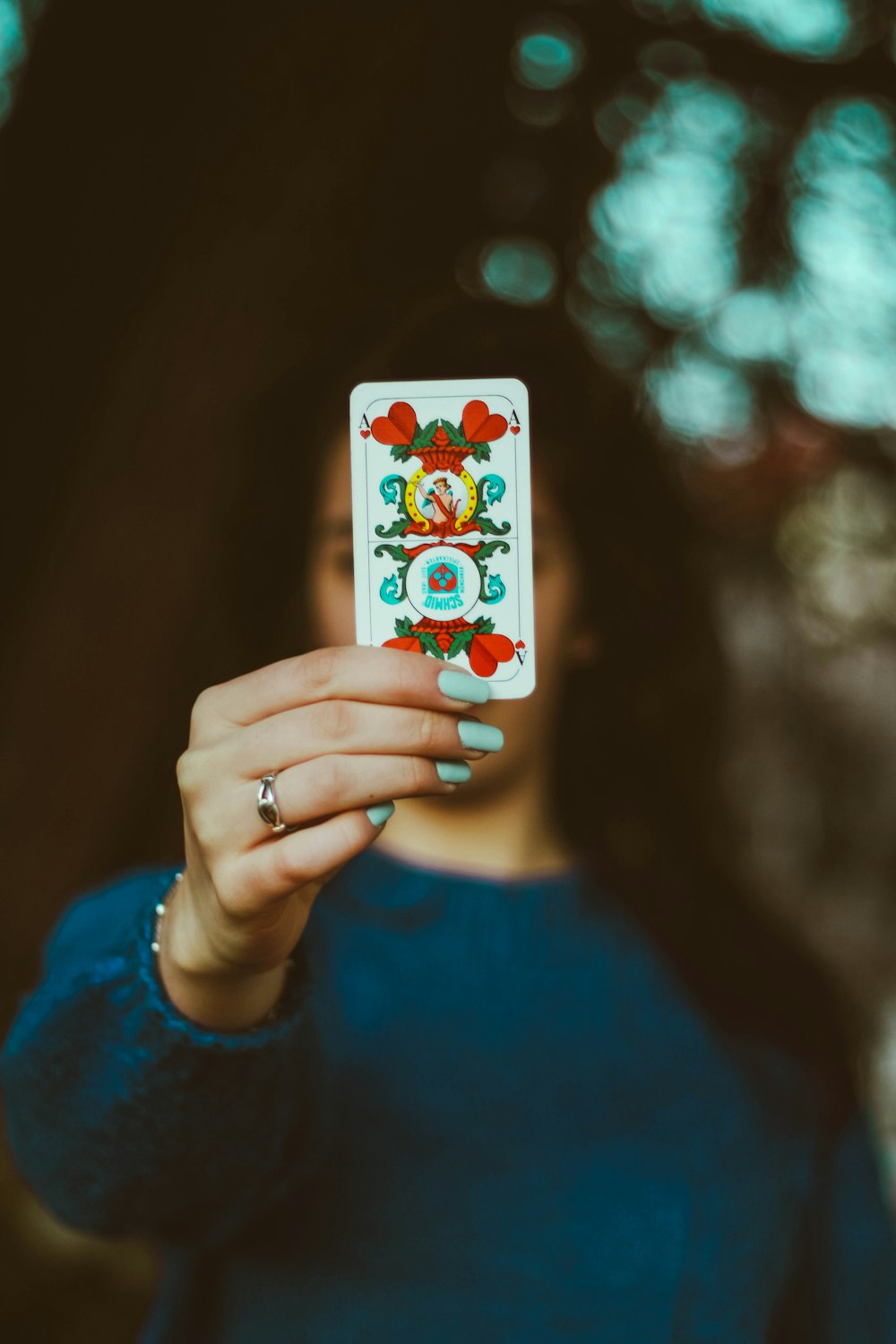 woman in blue crew neck shirt holding 6 of hearts playing card