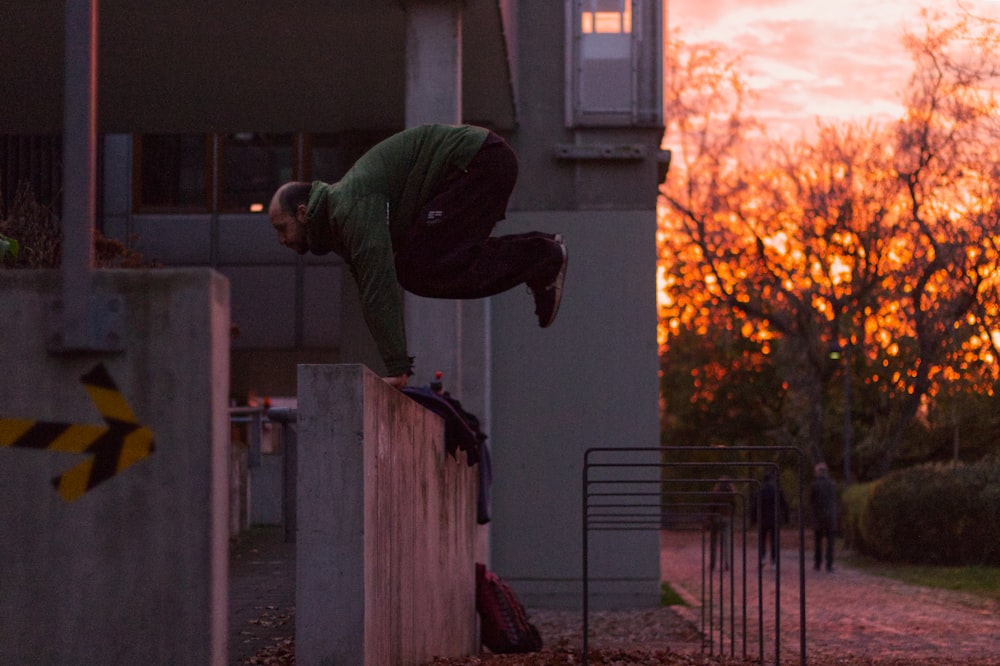 man in green jacket and black pants climbing on white wooden fence during daytime