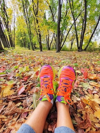 Close-up of colorful running shoes hitting a trail covered with autumn leaves.