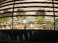 Model depicts the interior of a modern building, featuring several trees and seating areas. Multiple people are visible inside, engaged in various activities. The design of the building includes multiple horizontal lighted strips and a reflective glass facade that adds a dynamic feel.