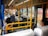 Inside a public bus, several passengers are seated, some wearing masks. The bus seats are blue with white head covers, and yellow poles and handles are visible. The bus appears to be in motion as the windows show blurred outdoor scenery.