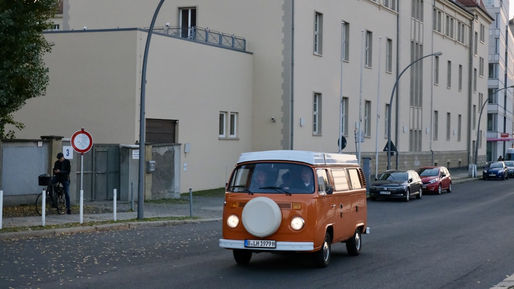 orange and white volkswagen t-2 parked beside white concrete building during daytime