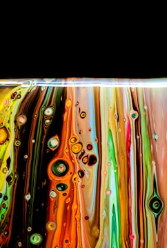Colorful vertically flowing paint layers with circular patterns and bubbles, reminiscent of abstract art. The colors blend together in vibrant streaks, with a dramatic black background at the top creating contrast.