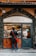 A person with a red sling bag stands in front of a traditional deli shop with a sign reading 'Antica Porchetteria Granieri 1916'. The shop window displays various bottles of wine and a selection of meats. Inside, a staff member wearing an apron and cap is attending to the customer.