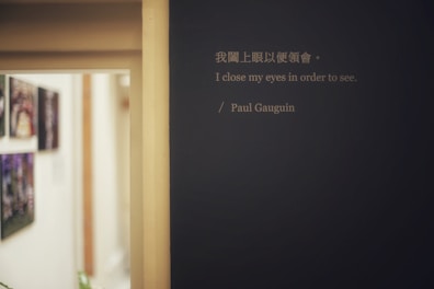 A hallway with abstract paintings hanging on the left wall is visible. A prominent quote by Paul Gauguin is displayed on a dark-colored wall, featuring both Chinese and English text. The lighting is soft, creating a calm and introspective atmosphere.