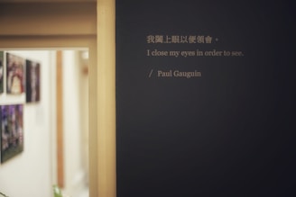 A hallway with abstract paintings hanging on the left wall is visible. A prominent quote by Paul Gauguin is displayed on a dark-colored wall, featuring both Chinese and English text. The lighting is soft, creating a calm and introspective atmosphere.