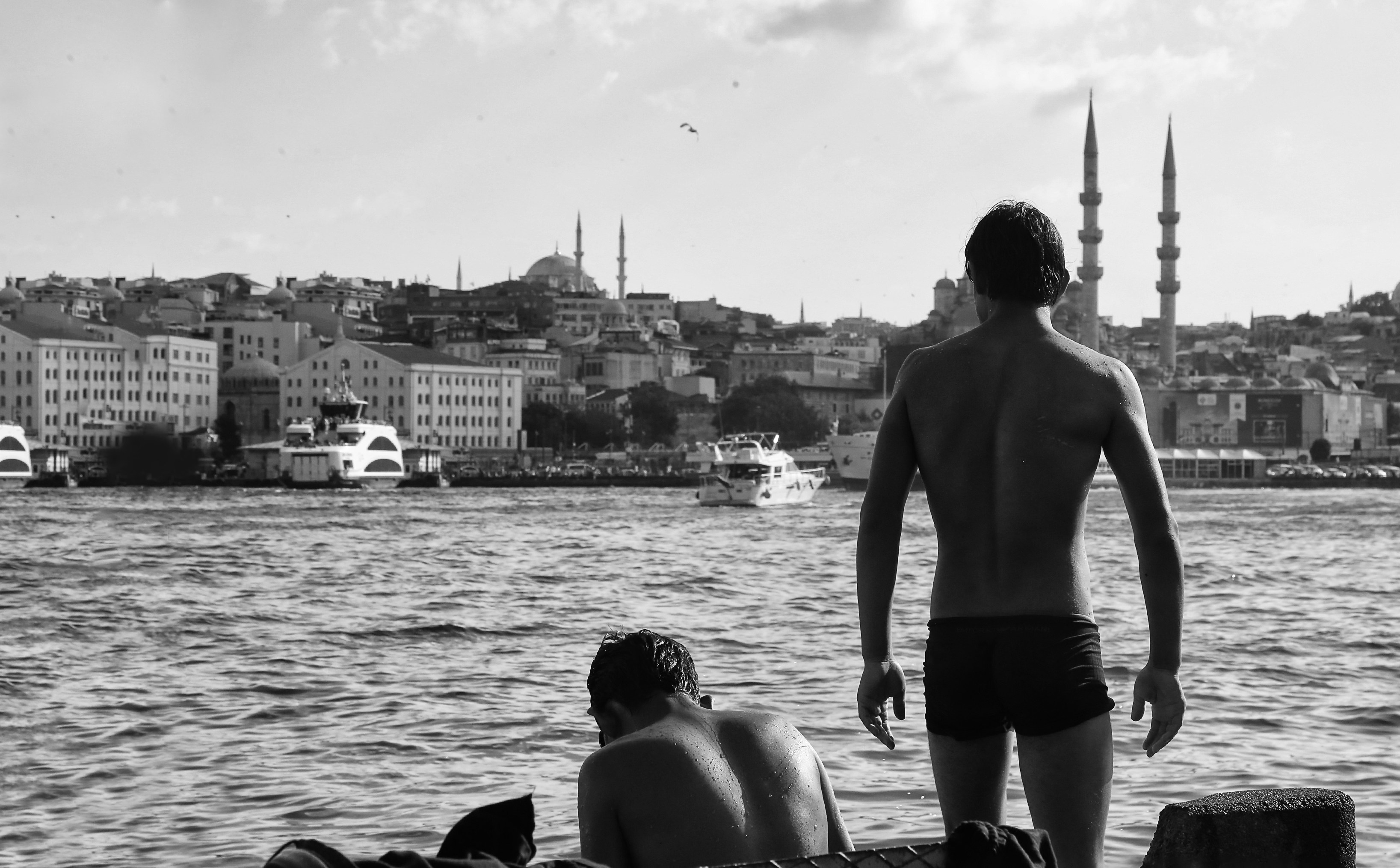 grayscale photo of 2 men standing on rock near body of water back teams background