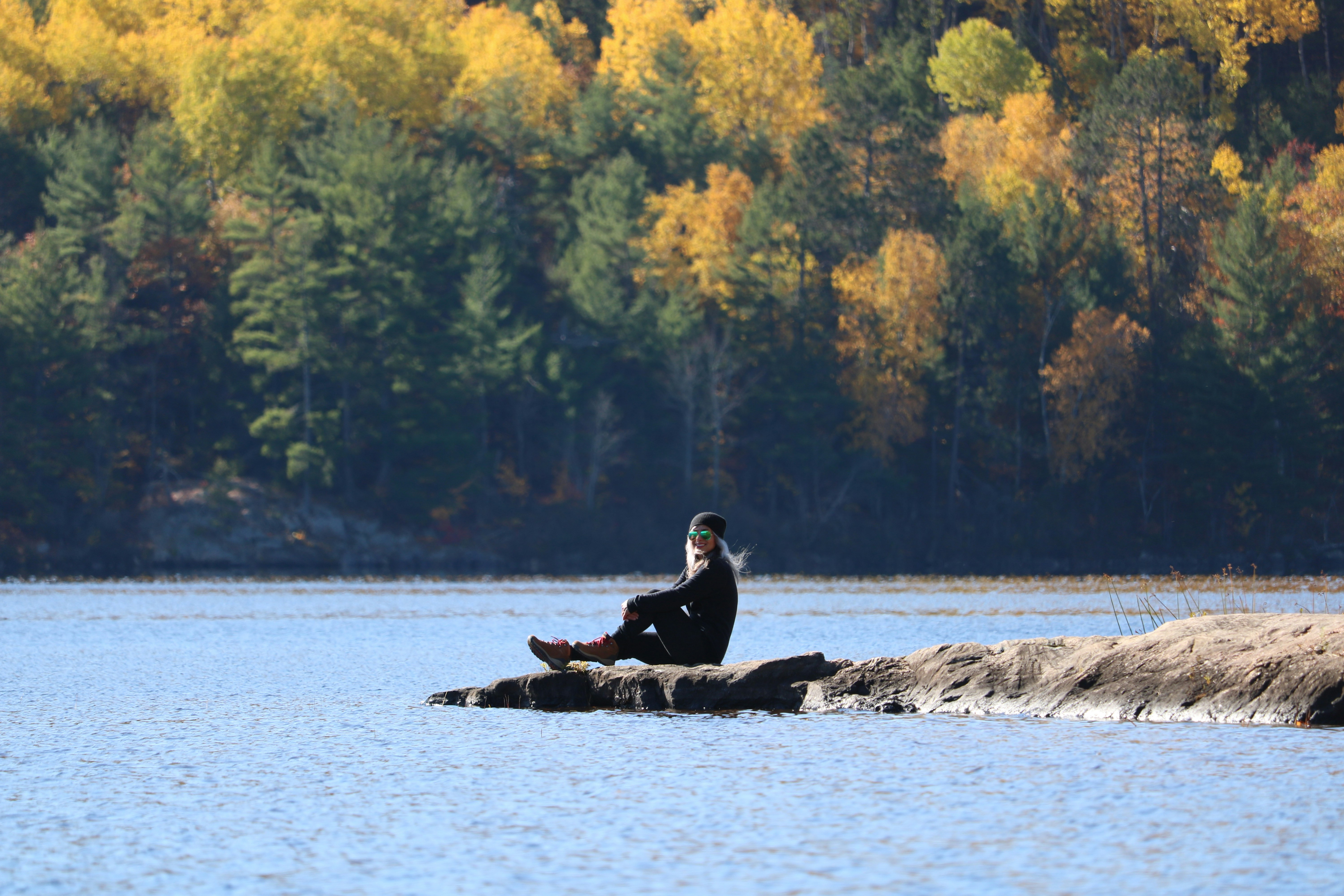 homme en veste noire assis sur le rocher au milieu de la mer pendant la journée