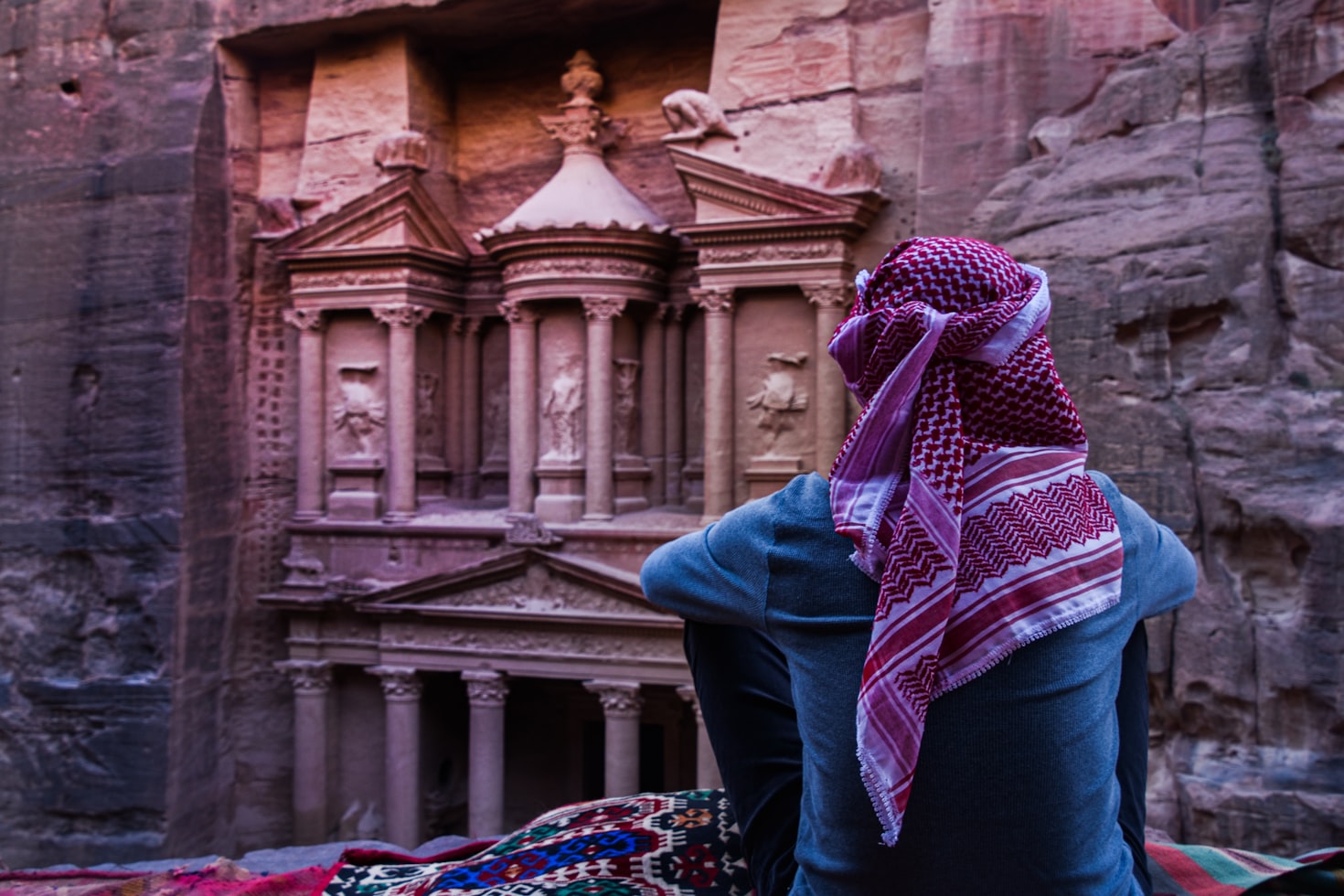 una persona col capo coperto guarda le rovine di Petra