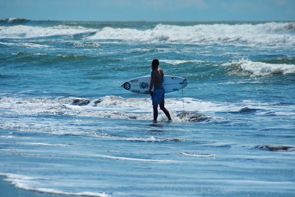 man in black shorts holding white surfboard walking on beach during daytime