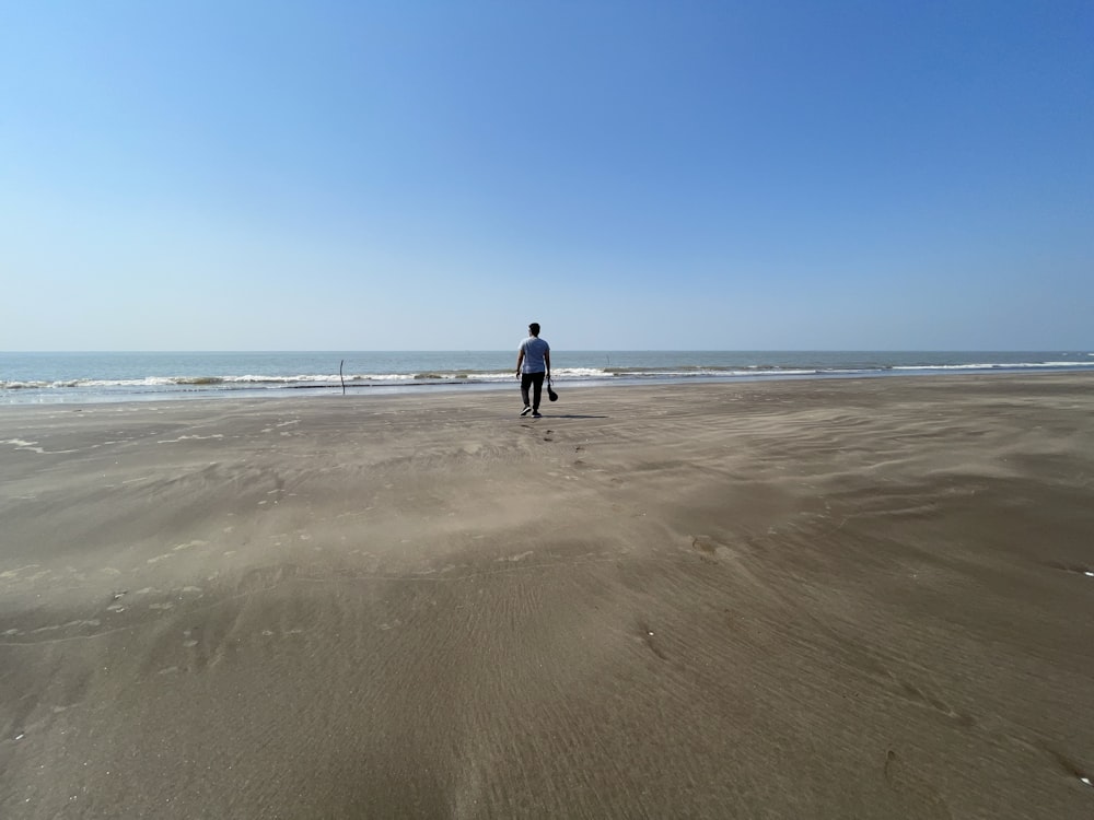 昼間、茶色の砂の上を歩く黒いジャケットの男