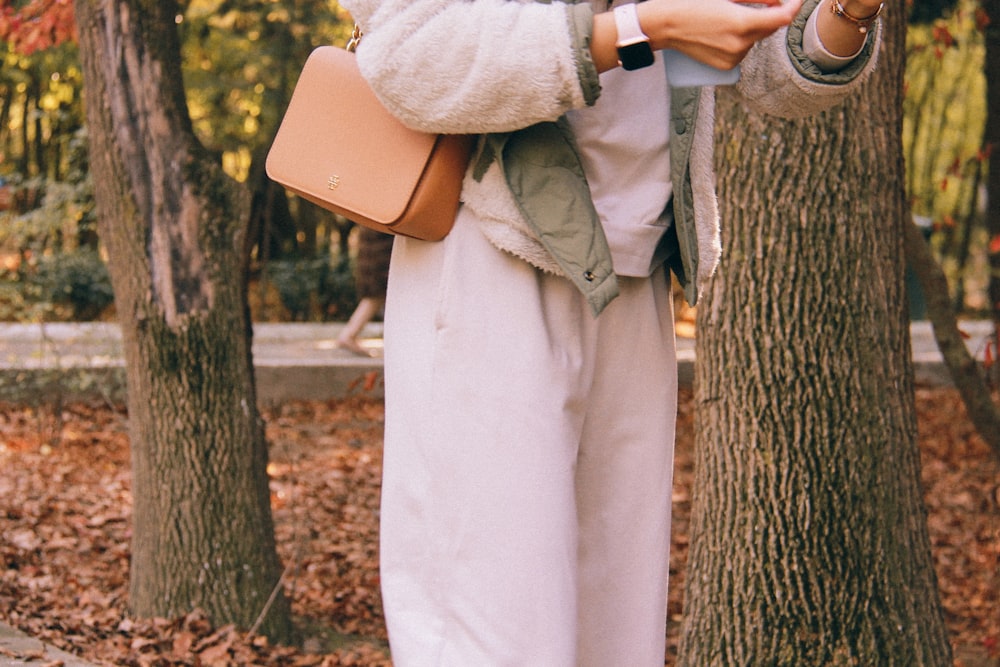 person in white dress shirt and brown pants holding brown leather bag