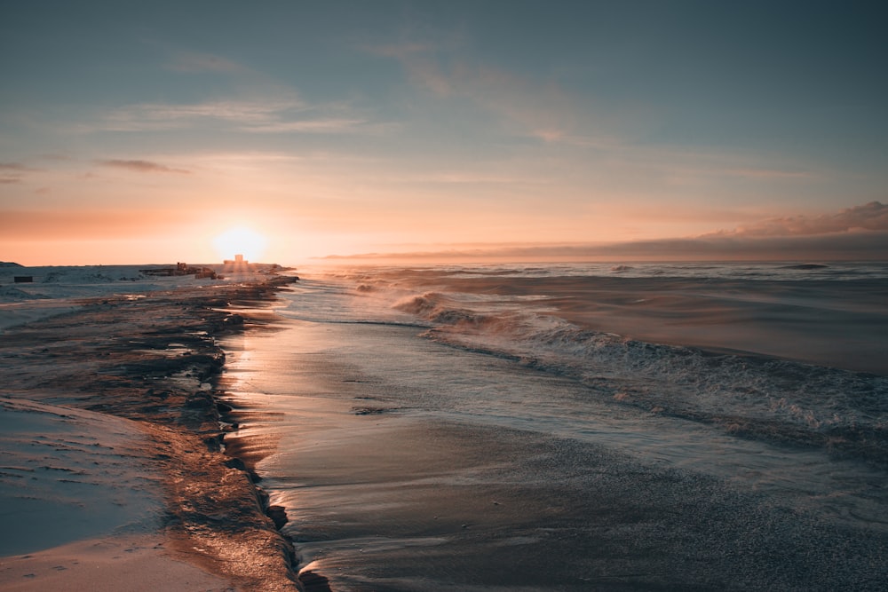 the sun is setting over the water on the beach