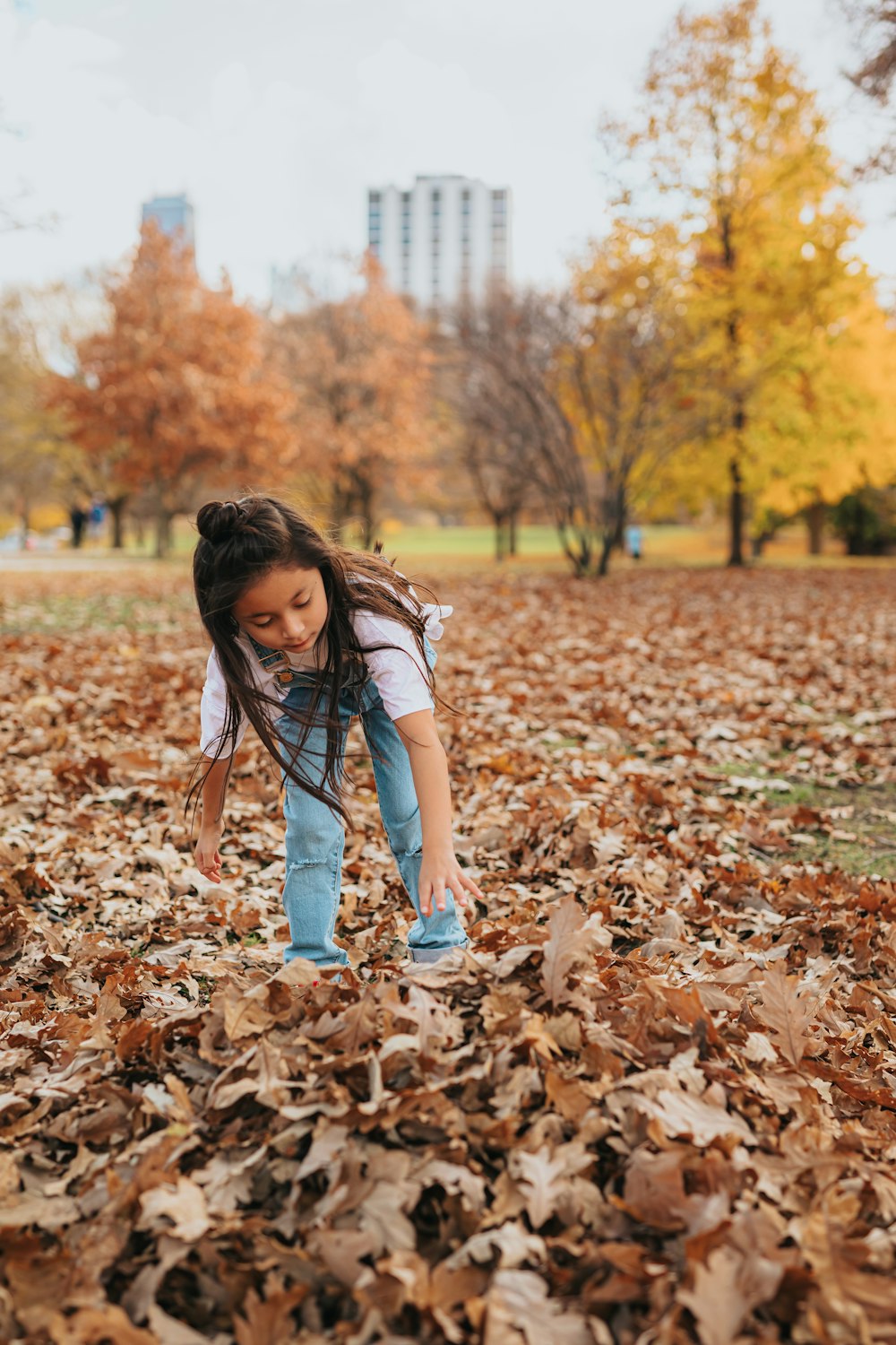 girl in white t-shirt and blue denim jeans standing on dried leaves during daytime