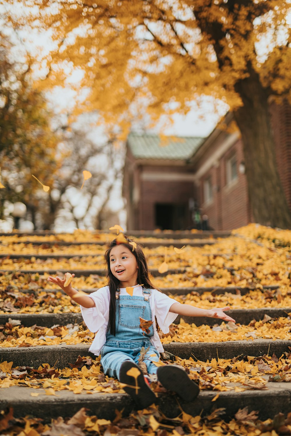 a little girl sitting on the steps in the leaves