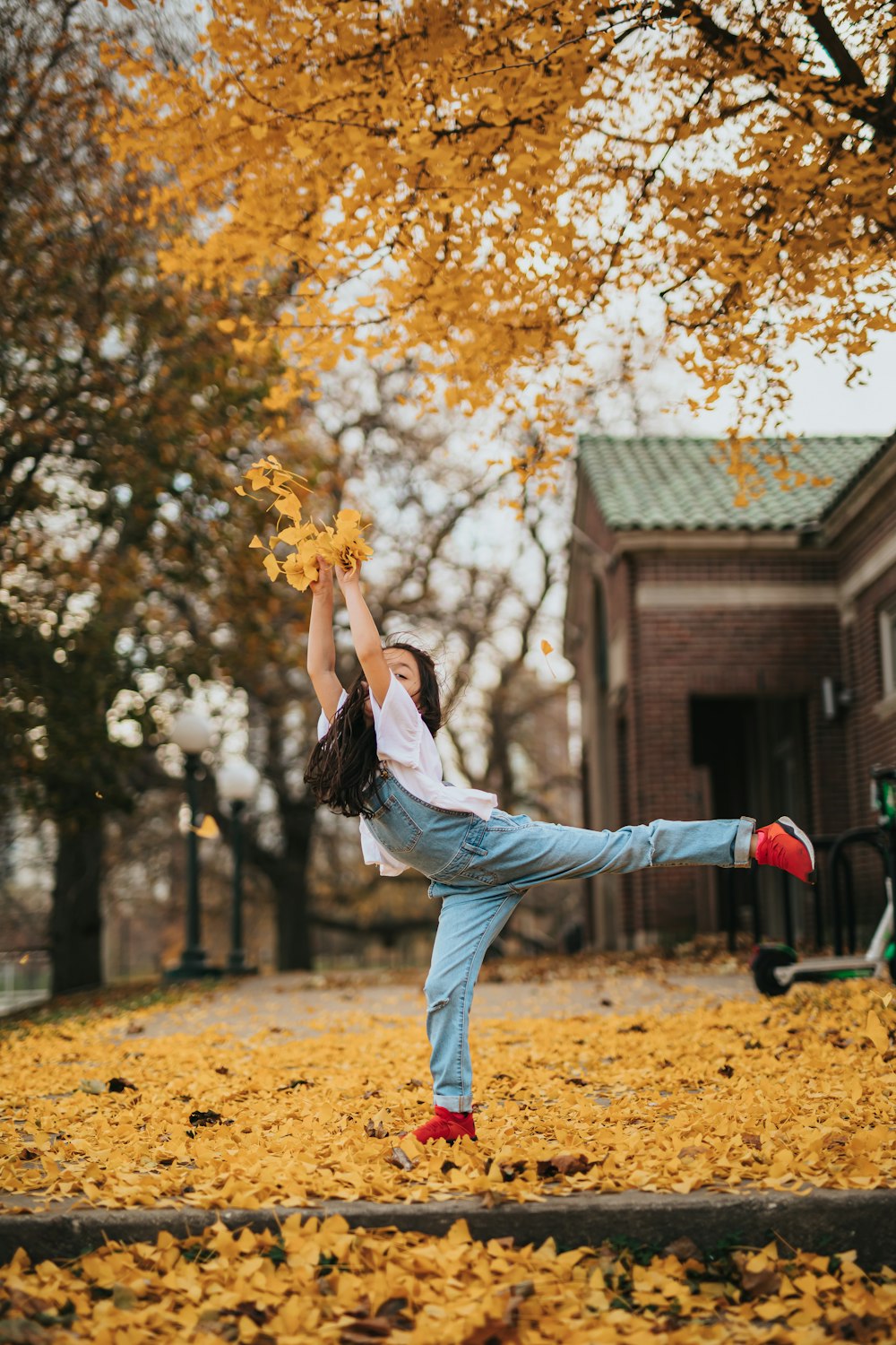 woman in white long sleeve shirt and blue denim jeans holding yellow maple leaf during daytime