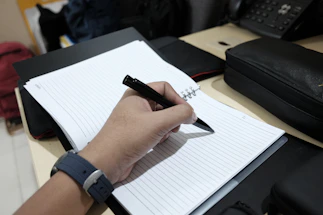 Close-up of a hand writing contact details on a clean desk with rubber samples nearby.