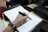 Close-up of hands writing in a sleek financial planner with a golden pen on a black desk.