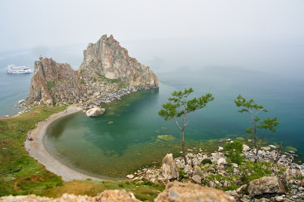green trees on rocky mountain beside body of water during daytime
